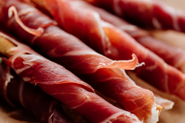 close up view of delicious sliced prosciutto wrapped around breadsticks - Fotografie, Obrázek