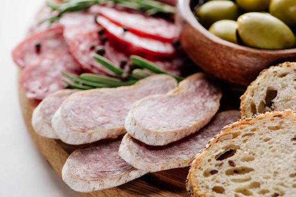 close up view of delicious sliced salami, bread and olives in bowl on wooden cutting board - Foto, immagini