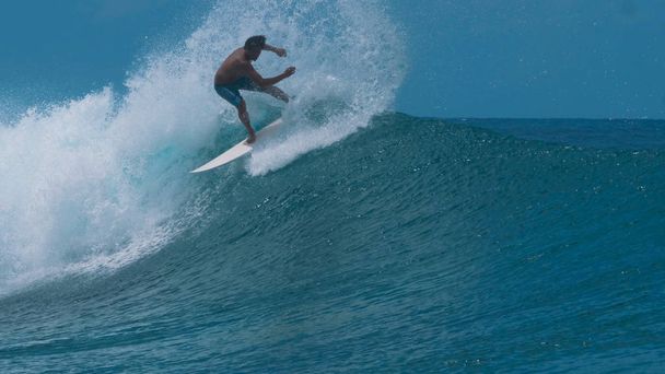 Κοντινό πλάνο: Pro surfer carves ένα μεγάλο σπάσιμο κυμάτων και σπρέι πεντακάθαρα ωκεανό νερού ψηλά στον αέρα. Εντυπωσιακό πλάνο της νεαρό αρσενικό surfboarder ιππασίας ένα επικίνδυνο κύμα στην ηλιόλουστη Γαλλική Πολυνησία. - Φωτογραφία, εικόνα