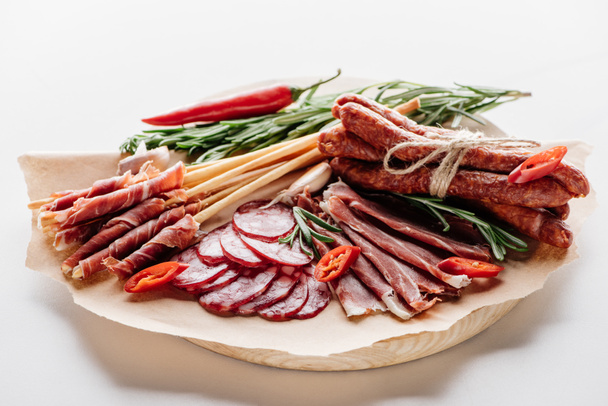 planche à découper ronde avec chili, herbes et délicieux salami, prosciutto et saucisses fumées sur papier d'emballage brun
 - Photo, image