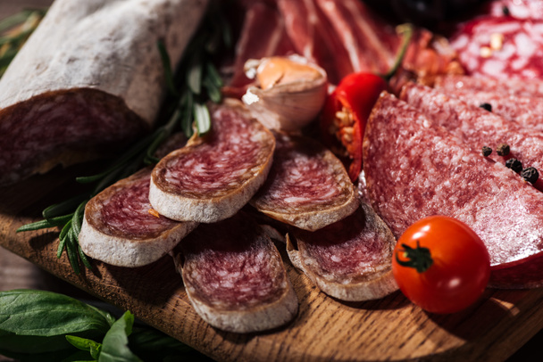 close up view of sliced salami with vegetables on wooden cutting board - Zdjęcie, obraz