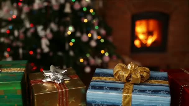 Sok karácsonyi ajándékok kandalló előtt, és homályos fények a karácsonyi fa az esti órákban - kamera csúszó - Felvétel, videó