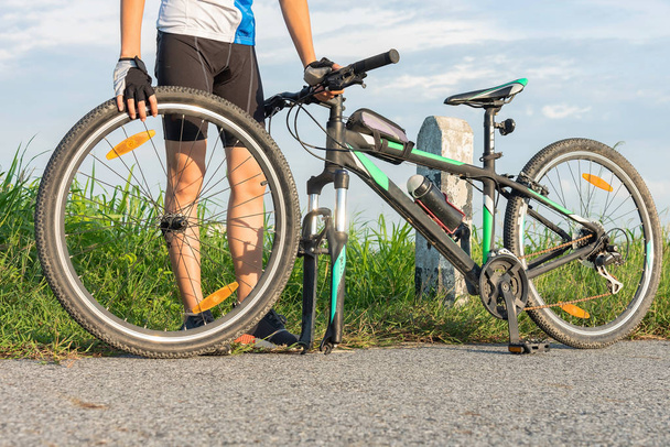  mulher ciclista de bicicleta em apuros de roda de pneu dianteiro precisa de reparação e ajuste por si mesma na estrada
 - Foto, Imagem