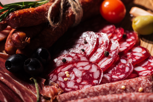 close up view of delicious sliced salami with vegetables and spices on wooden cutting board - Photo, Image
