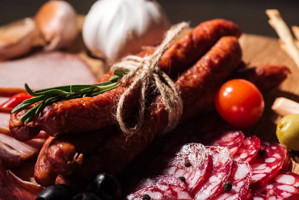 Ahşap kesme tahtası lezzetli dilimlenmiş salam, füme sosis, otlar ve sebze ile görünümünü kapat - Fotoğraf, Görsel