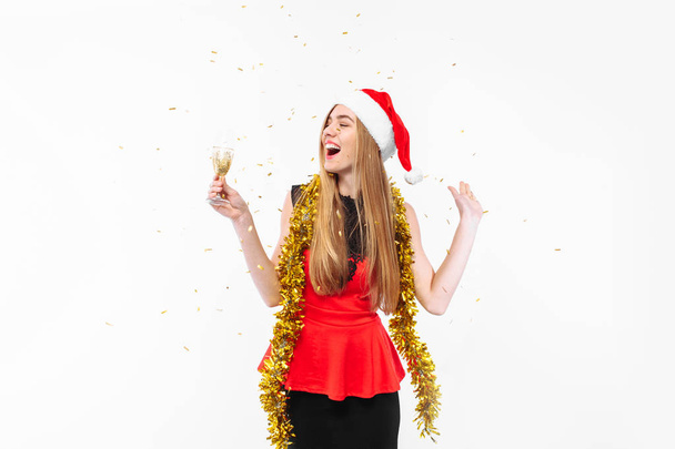 Happy young woman wearing a dress and Santa hat, celebrating the new year, in her hands, a glass of champagne, on a white background. Christmas concept. - Fotó, kép