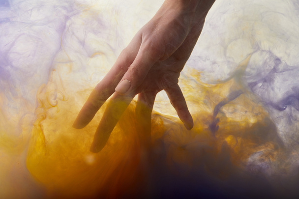 περικοπεί άποψη του χέρι σε νερό με πορτοκαλί και μοβ χρώμα  - Φωτογραφία, εικόνα