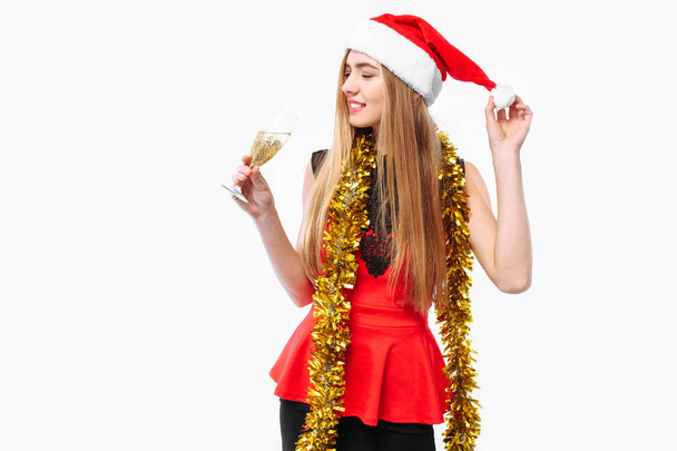 Happy young woman wearing a dress and Santa hat, celebrating the new year, in her hands, a glass of champagne, on a white background. Christmas concept. - Foto, immagini