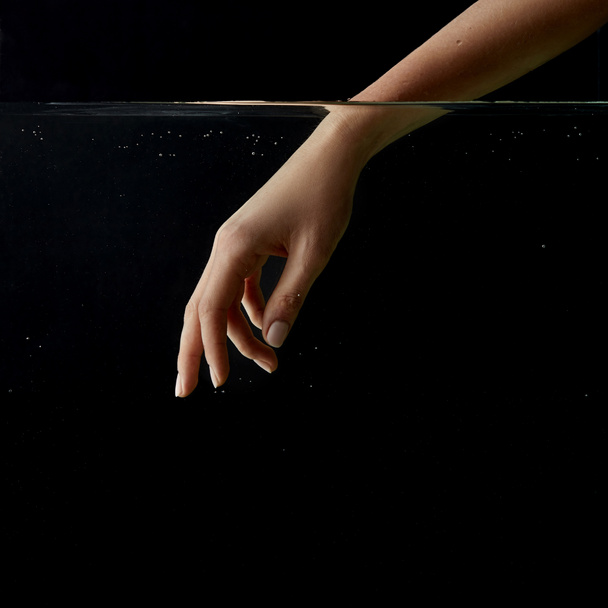 partial view of girl putting hand into clear water isolated on black  - 写真・画像