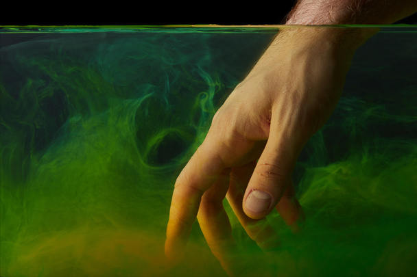 Μερική άποψη των αρσενικών χέρι σε νερό με πράσινο χρώμα στροβιλίζεται - Φωτογραφία, εικόνα