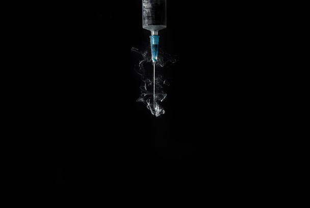 syringe with smoke or paint swirls isolated on black - Foto, Bild