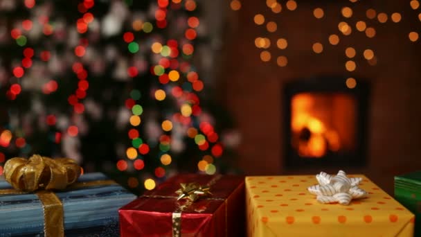 viele Weihnachtsgeschenke vor dem Kamin und verschwommene Lichter am Weihnachtsbaum am Abend - Kamera rutscht - Filmmaterial, Video
