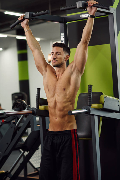 Attractive fitness guy doing pull-up on the crossbar during training in the modern gym. Close up shot. - Foto, Imagem