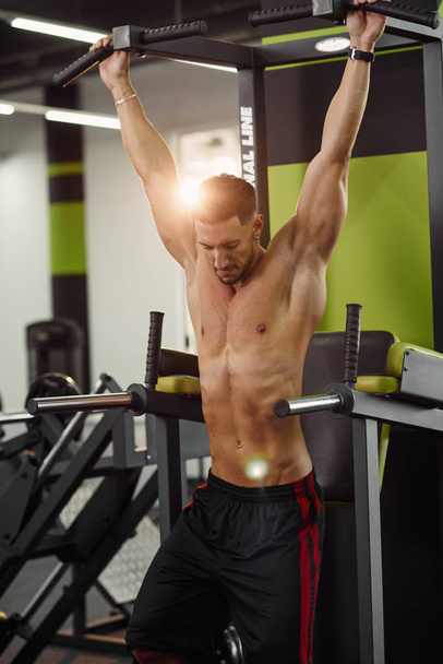 Attractive fitness guy doing pull-up on the crossbar during training in the modern gym. Close up shot. - 写真・画像