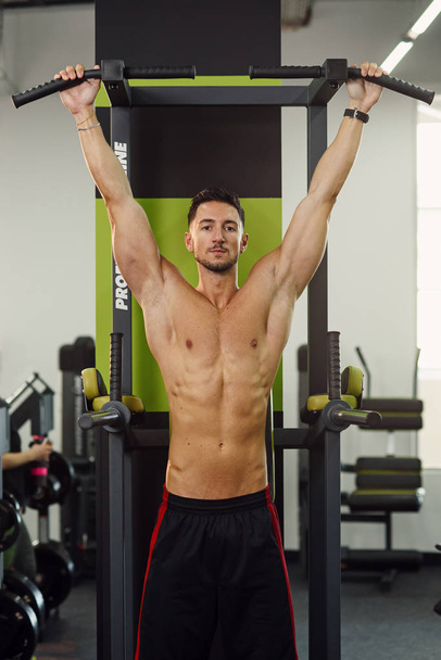 Strong attractive man does pull-up on the crossbar during training in the modern gym. Front view. - Fotoğraf, Görsel
