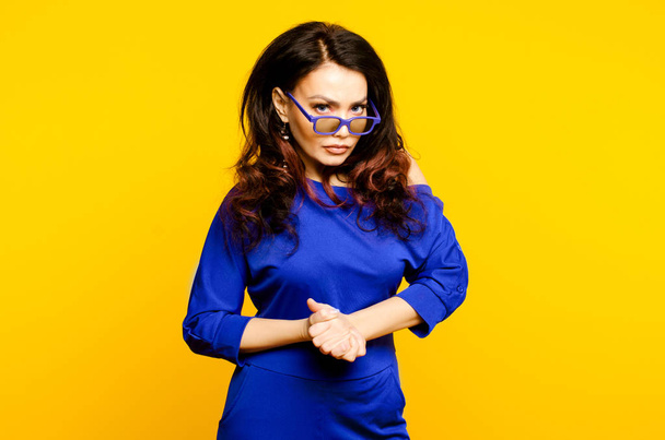 Very angry businesswoman in blue suit and glasses looking to camera, isolated on yellow - Foto, afbeelding