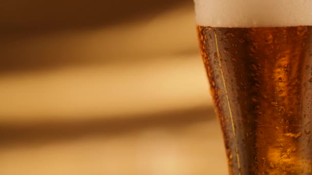Nahaufnahme von rotierendem frischem Bier mit abstraktem goldenem Hintergrund und Tropfen auf Glas - Filmmaterial, Video