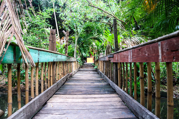 Old wooden suspension bridge used to cross the stream. The trees and plants are full - Photo, Image