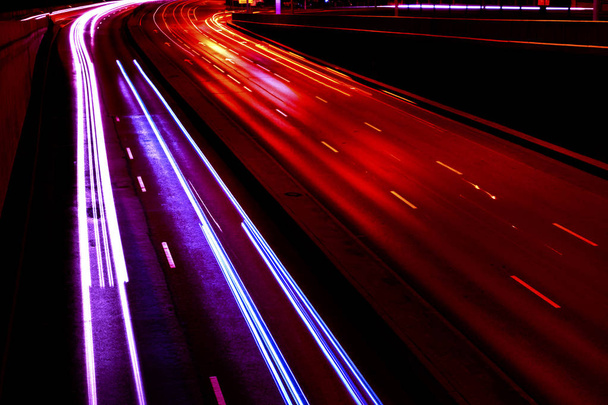 Cars light trails on a curved highway at night. Night traffic trails. Motion blur. Night city road with traffic headlight motion. Cityscape. Light up road by vehicle motion blur. - 写真・画像