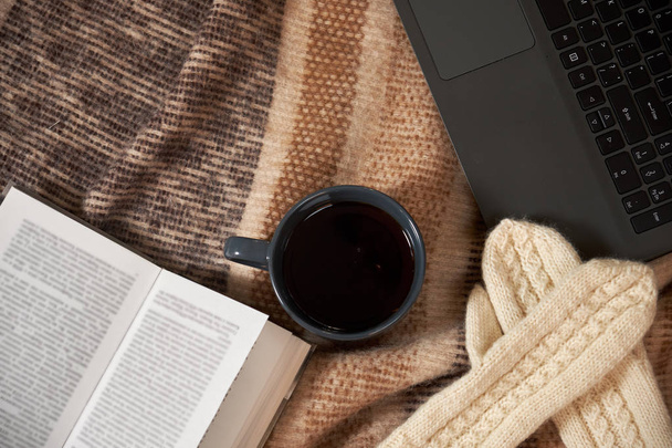 Een kopje thee, een boek, een laptop en wanten op een deken - Foto, afbeelding