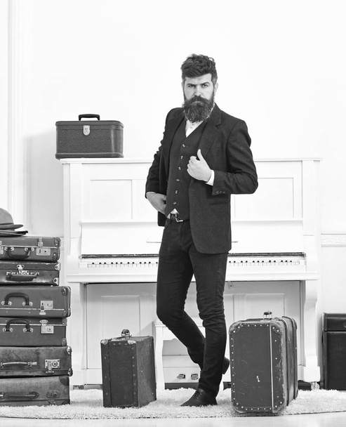 Man, traveller with beard and mustache with luggage, luxury white interior background. Macho elegant on strict face standing near pile of vintage suitcase. Luggage and travelling concept - Foto, immagini