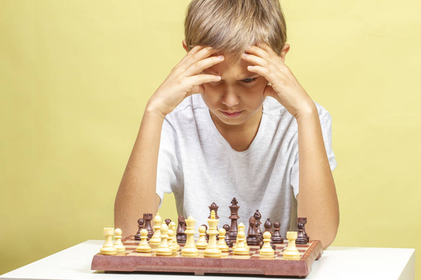 Парень играет в шахматы. Мальчик смотрит на шахматную доску и думает о своей стратегии
. - Фото, изображение