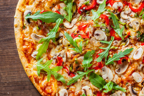 Vegetarische Pizza met Mozzarella Kaas, champignons, tomatensaus, peper, specerijen en verse rucola. Italiaanse pizza op houten tafel achtergrond - Foto, afbeelding