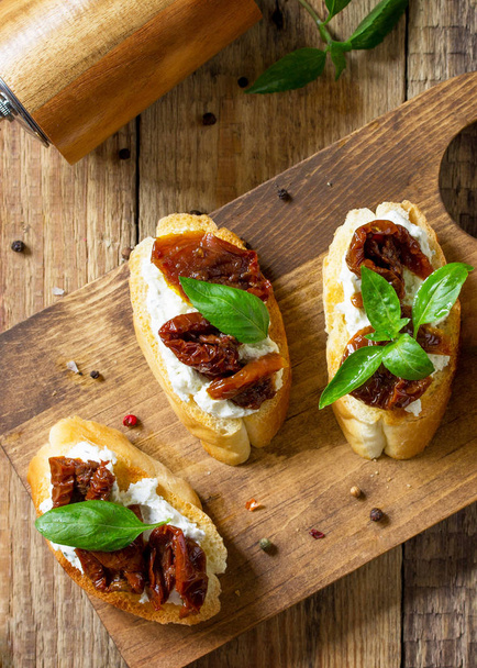 Italian Antipasti-välipaloja viinille. Harjat pehmeällä juustolla ja kuivatuilla tomaateilla puupöydällä. Top view tasainen lay tausta
 - Valokuva, kuva