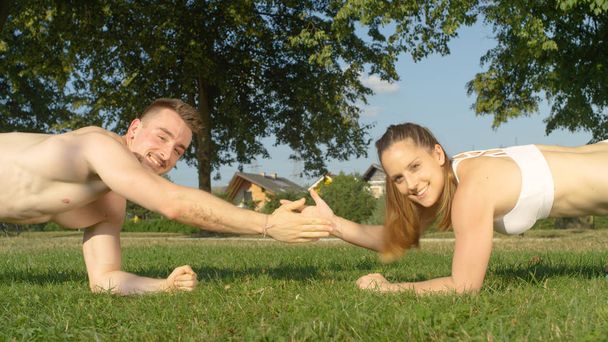 Porträt: junges sportliches Paar High Fives beim Training draußen in der Sonne. fit kaukasische Freundin und Freund genießen die Bewegung im Park und klatschen in die Hände, während ihr Bauch trainiert. - Foto, Bild