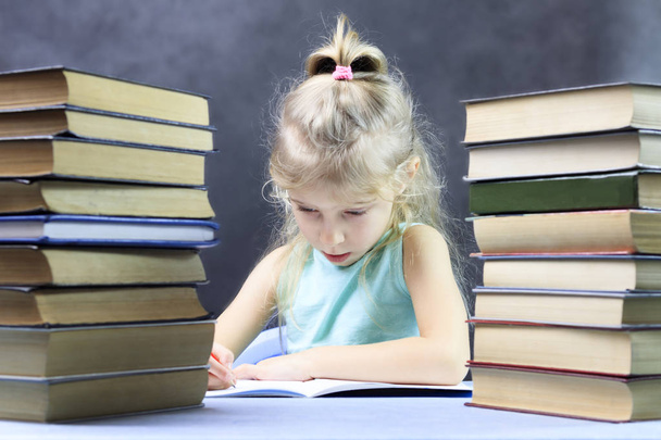 Schoolmeisje, blond meisje met een stapel boeken en een potlood schrijft in een notitieblok. Er is toning. - Foto, afbeelding