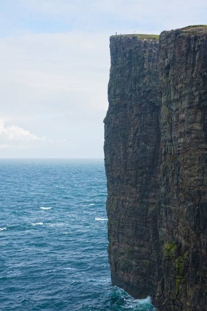 AEREO: Volando sopra l'oceano blu e verso una scogliera rocciosa mozzafiato nelle Isole Faroe. Splendida foto di un piccolo turista in piedi sulla cima dell'incredibile scogliera che sovrasta il mare infinito
. - Foto, immagini