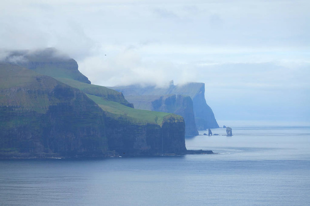 AERIAL: Flying over the calm ocean and towards the black cliffs of a spectacular islet in the picturesque seaside of Faroe Islands. Spectacular view of the rugged Scandinavian shoreline on cloudy day. - Photo, Image