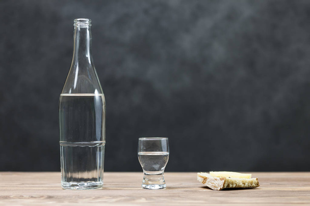 a glass of pure alcohol, a bottle and a piece of bread and cheese on a wooden background. a glass and on it a red cross. concept of quit drinking. there is toning. - Фото, изображение