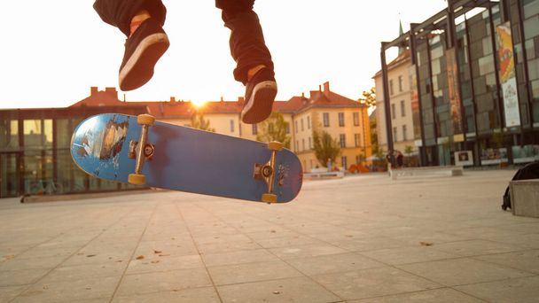 LOW ANGLE, CLOSE UP: Синій скейтборд під ногами молодих і спортивних скейтбордистів. Невпізнаваний чоловічий скейтбординг і трюки на міських вулицях на ідилічному осінньому вечорі
. - Фото, зображення