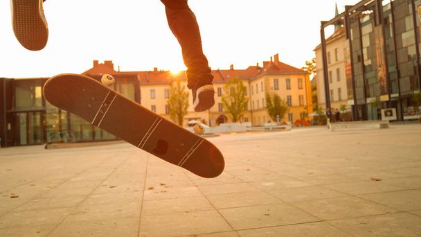 Zbliżenie, niski kąt, soczewka flary: nieznany sportowiec Skater robi Flip trick na słonecznej jesieni wieczorem. Nierozpoznawalny młody męski Skateboarding i robi fajne sztuczki na zapierającym dech w piersiach pomarańczowym zachodzie słońca - Zdjęcie, obraz