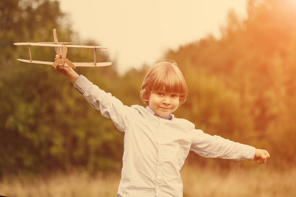 Aviador piloto infantil con avión al atardecer, niño jugando con el avión de juguete de cartón al aire libre, contra el fondo del cielo de verano. Retro tonificado. sueños de viajar
 - Foto, Imagen