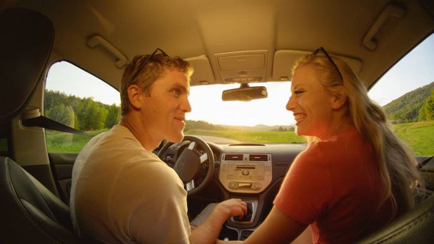クローズ アップ: 幸せな女と男、牧歌的な夏の夜の美しい田園地帯を通って運転している間互いの目を見てします。風光明媚を楽しんでいる陽気なカップルは田舎道をクルーズします。 - 写真・画像