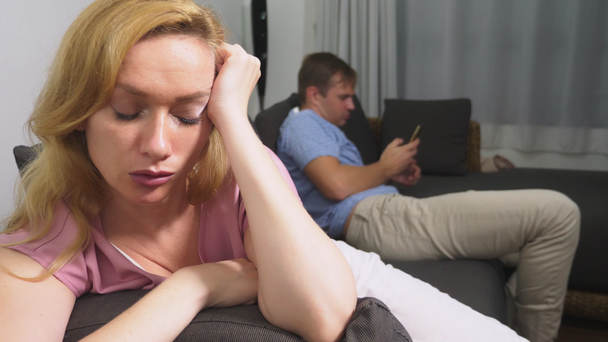 Couple crisis. Man and woman spend the evening in the living room on the couch. the man uses the phone, the woman is upset that he does not pay attention to her - Footage, Video