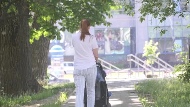 young mother moving away with pushing baby carriage. 4K slow mo - Záběry, video
