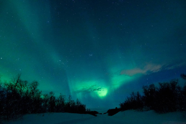 Πολύχρωμο Βόρεια φώτα λαμπερό πέρα από την όμορφη έρημο κρύους και χιονώδεις στη Φινλανδία. Εντυπωσιακό πλάνο του νυχτερινού ουρανού ακριβώς όπως το διάσημο Βόρειο σέλας που εμφανίζεται πάνω από την τραχιά χειμερινό τοπίο - Φωτογραφία, εικόνα