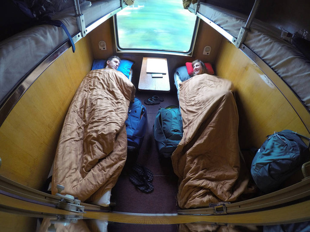 Onnellinen valkoihoinen matkustaja pari makaa sängyssä lämpimien peittojen alla ratsastaessaan nukkuva juna kulkee Vietnamissa. Iloinen nuori mies ja nainen lepää matkalla lomakohteeseensa
. - Valokuva, kuva