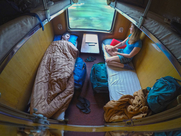 Mannelijke en vrouwelijke backpackers rusten onderweg in een trein cool slaper. Man ligt in bed, terwijl zijn vriendin zitten en op zoek door het raam tijdens een treinreis over Vietnam. - Foto, afbeelding