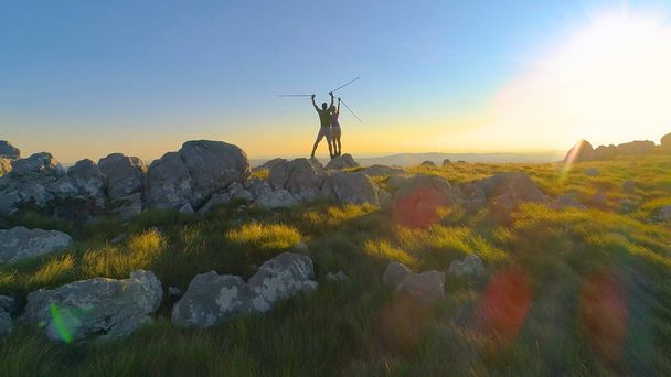 スロベニアの山の頂上に到達を祝う 2 つのアクティブな観光客にレンズフレアのエアリアル: 飛行。美しい夏の太陽光線の見事な自然観察、陽気な白人カップルに輝き - 写真・画像