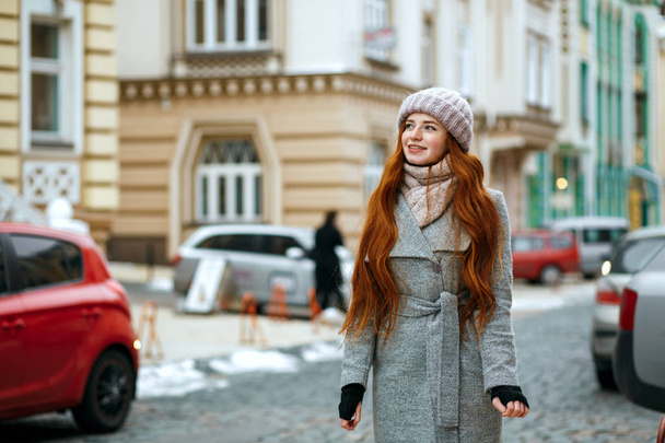 Magnificent red head woman wearing winter cap and coat pwalking at the city. Space for text - Foto, afbeelding