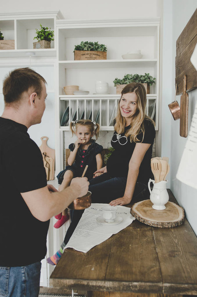 happy young family with pregnant woman and little girl sitting in scandinavian kitchen and having fun - 写真・画像