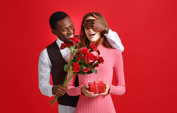 valentine's day concept. happy young couple with heart, flowers, gift on red backgroun - Photo, Image