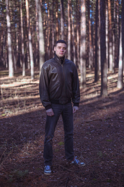 Un joven de aspecto criminal en una chaqueta de cuero negro posando en un bosque otoñal
 - Foto, Imagen