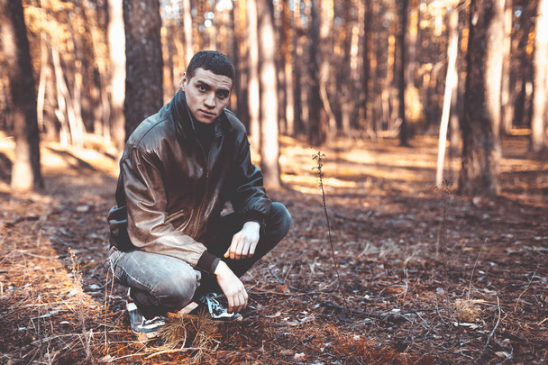 Un giovane uomo di aspetto criminale in una giacca di pelle nera in posa in una foresta autunnale
 - Foto, immagini