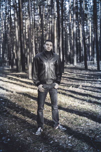 Egy fiatal férfi, bűnügyi megjelenés a fekete bőr kabát, az őszi erdő pózol - Fotó, kép