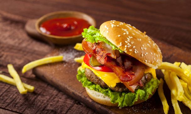 frische köstliche Burger mit Rindfleisch, Tomaten, Käse, Gurken, Zwiebeln und Salat auf Holz Hintergrund - Foto, Bild